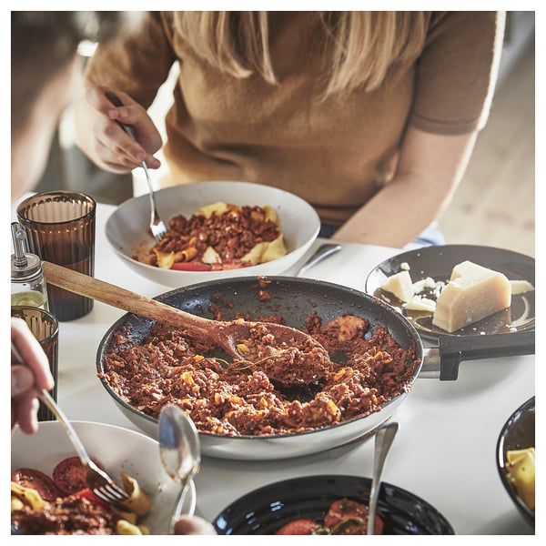En kvinde serverer solid kødret i en stor stegepande på et spisebord med forskellige tilbehør og et glas øl.