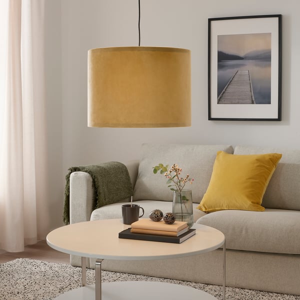 Moderne stue med gul MOLNSKIKT lampe over beige sofabord. Varmglødende fløjlslampe hænger over sofaen med gul pude, under vægkunst.