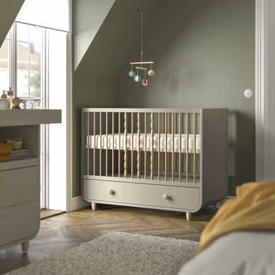 Moderne børnehave med grønne vægge. Grå og træfarvet MYLLRA-seng, mindre end nærliggende kommode, med uro ovenover.