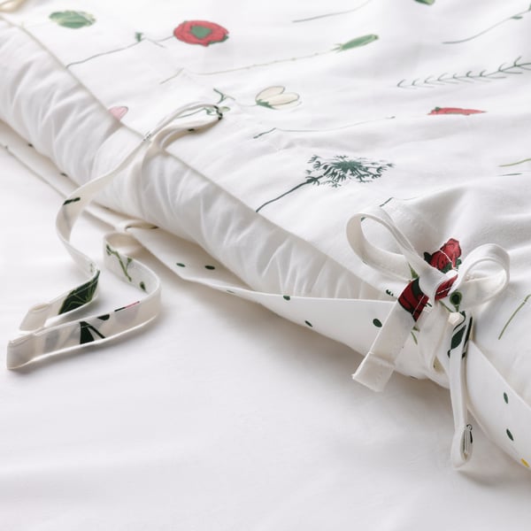 Hvidt dynebetræk med blomstermønster, båndbånd og prikker på bagsiden, lagt ud på en seng.