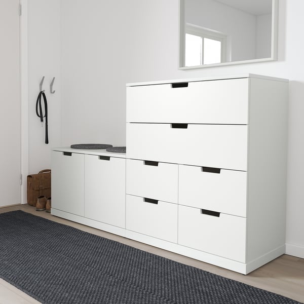 Moderne hvid NORDLI kommode i entreen, med gråt tæppe. Høj enhed med seks skuffer og sorte håndtag, placeret ved kroge og bænk.