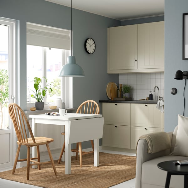 Moderne køkken med NORDVIKEN bord, stole, blå pendel og sort ur. Beige sofa med lyseblå vægge og potteplante.