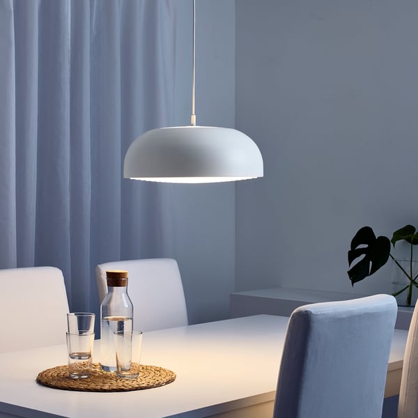 Moderne spiseplads med hvide stole omkring et bord under en pendel. En vandkaraffel og glas står på bordet.