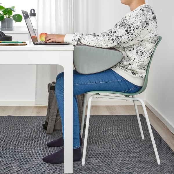Person, der sidder ved et skrivebord, bruger en bærbar computer og fodstøtte til at støtte fødderne og opretholde en god kropsholdning.