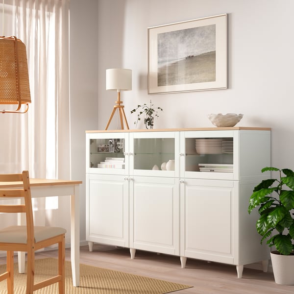 Hvidt OSTVIK skab med glaslåger i minimalistisk stue, flankeret af en lampe og plante.
