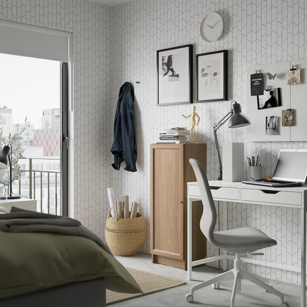 Pænt hjemmekontor med OXBERG reol, hvidt skrivebord og stol, geometrisk tapet og stort vindue med udsigt over byen.