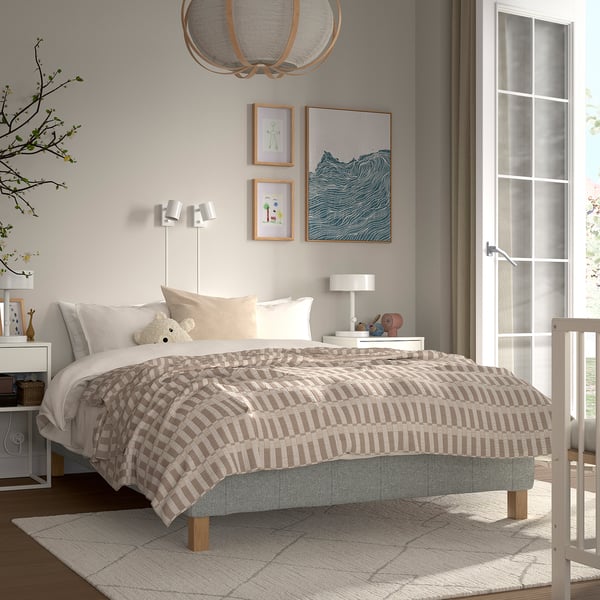 Hyggeligt soveværelse med RENFJÄLLET seng, beige-hvidt sengetøj, lille legetøj, moderne kunst, varmt tæppe.