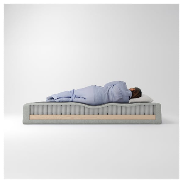 En person, der sover på en madras med synlige indre spiraler, bestående af lag af polyester, polyurethanskum, stålfjedre og fyrretræsbundelementer.