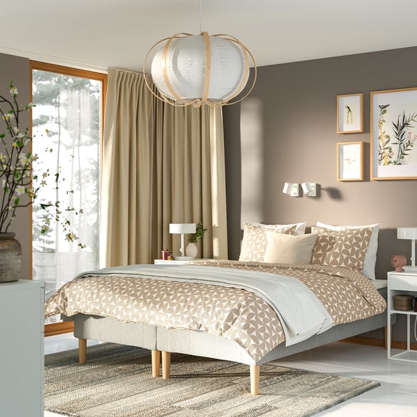 Moderne neutralt soveværelse: stor seng med beige geometrisk sengetøj, natborde i træ, hængende lampe. Gardiner og tæpper supplerer indretningen.