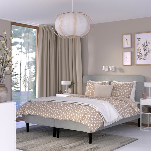 Moderne soveværelse med beige sengetøj, geometriske prints, unik lampe og potteplante.