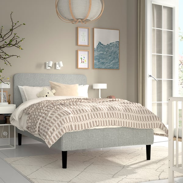 Minimalistisk soveværelse med RENFJÄLLET seng, sorte ben, hvid sengegavl, ternet tæppe, lys, kunst, sidelampe, stort vindue, råhvidt tæppe.