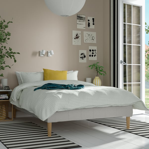 Moderne soveværelse med RENFJÄLLET-seng, gul pude, minimalistisk kunst, stribet tæppe, glasdør.