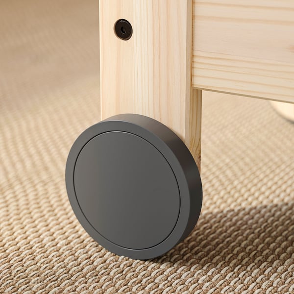 Mørkegrå, rund gulvlås på træmøbelben, tæppebelagt gulv.