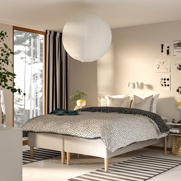 Moderne soveværelse med RISHÖJDEN kingsize-seng, hvid sengegærde, sort/hvidt sengetæppe, pendelampe, tæppe, plante og abstrakt kunst.