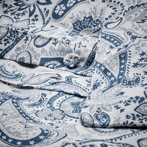 Foldet paisley-mønstret sengetøj med blå og hvide nuancer, der viser indviklede blomsterdesigns, pænt lagt ud.