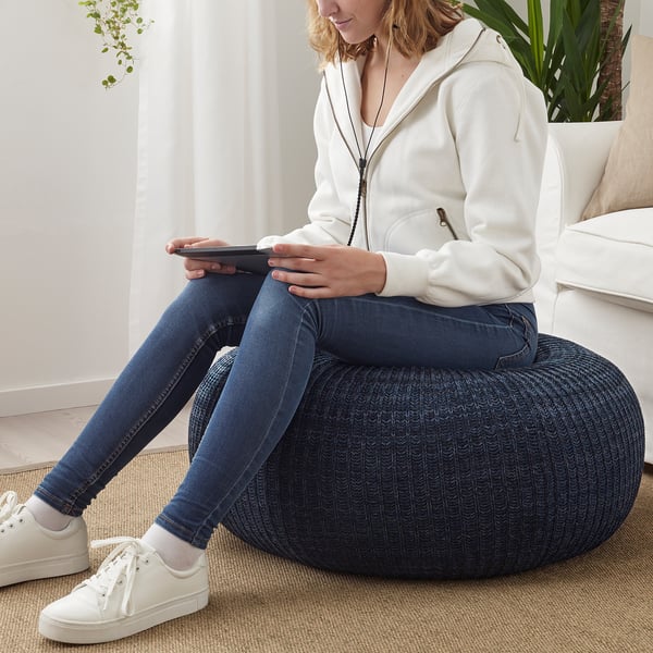 Person, der sidder på blå puffe, bruger tablet og er iført hvid hættetrøje, jeans og sneakers.