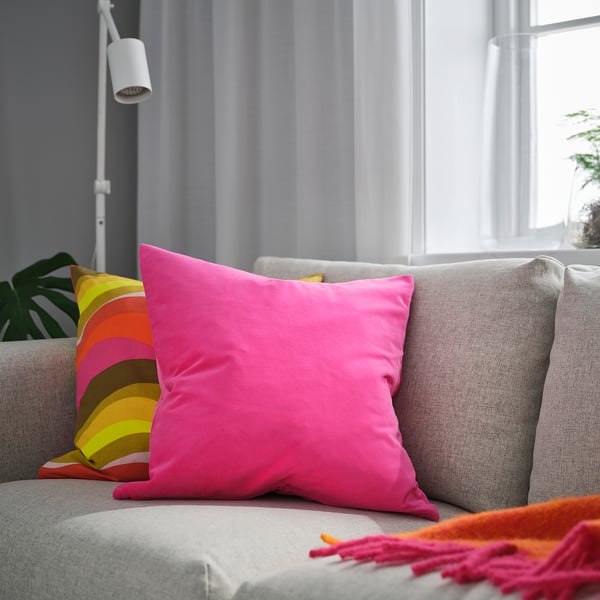 Lyserød SANELA pude på en neutral sofa, stor, plys, firkantet.