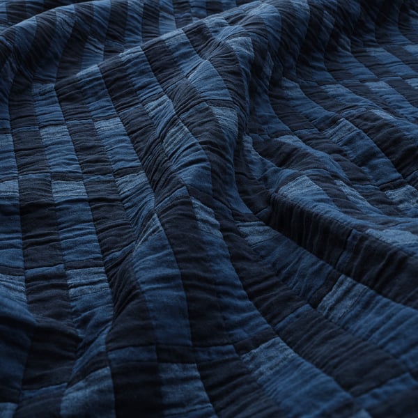 Mørkeblå quilt med synlige syninger, pænt foldet, der viser kvalitetsstof og håndværk.