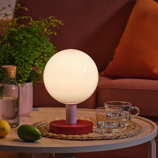 Rund lampe på bordet med kopper og frugt. Blødt lys oplyser hyggelige omgivelser.