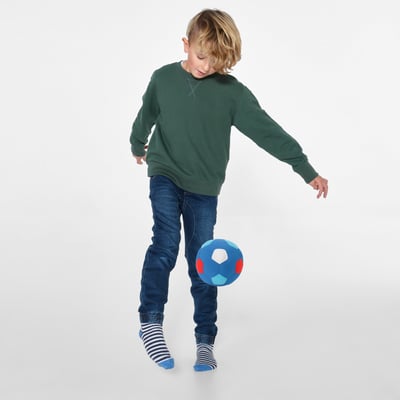 Barn balancerer farverig bold på knæet, iført grøn sweater, jeans og stribede sokker.
