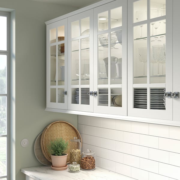 Hvidt køkkenskab med glasdøre, der viser tallerkener, planter og krukker. Pletafvisende og moderne design.