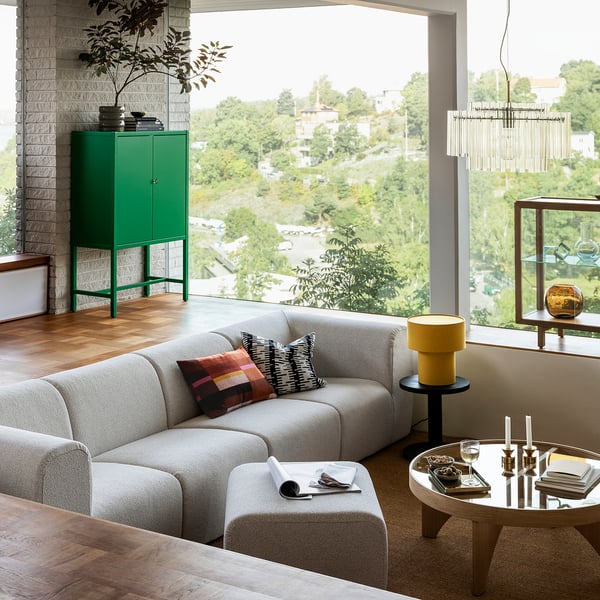 Moderne stue STOCKHOLM 2025 sofa i neutralt stof, store vinduer, grønt skab, trægulv. Hyggeligt, rummeligt, med naturligt lys.