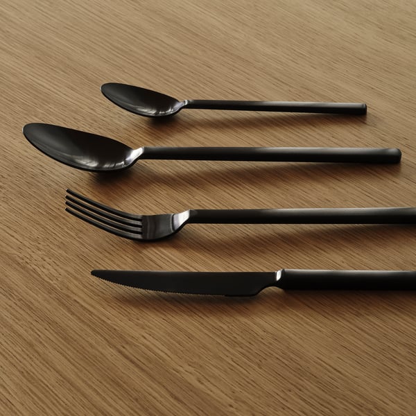 Fire moderne bestikstykker lagt pænt på træoverfladen. Mørk finish i rustfrit stål, slankt design.