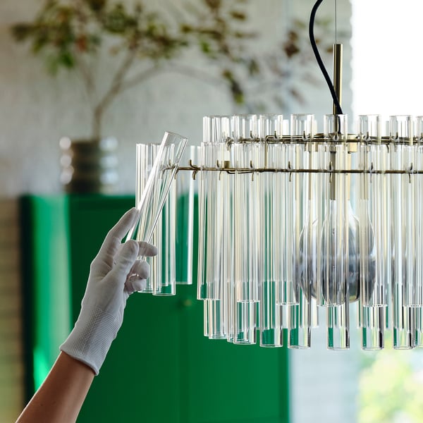 Håndjusterer moderne lysekrone med glasrør og messingkroge, der fastgør lyspositionen.