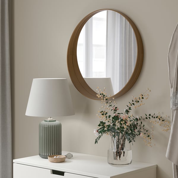 Cirkulært spejl på væg, skrivebord med grøn lampe og vase.