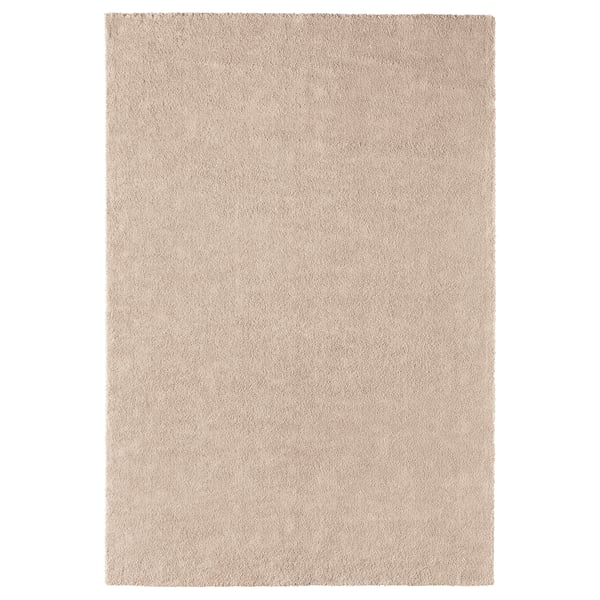 Et beige ikea STOENSE tæppe med en blød, tyk luv, der giver komfort og varme. Den har en let glans, rektangulær form og en glat kant.