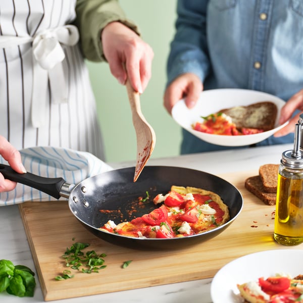 To personer laver mad sammen; Man bruger en let stegepande med et let greb til en tomat- og osteskål.
