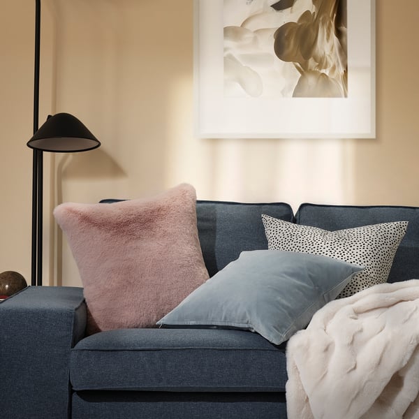 Stue med grå sofa, lyserød pude, sort lampe, abstrakt kunst.