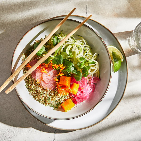 En skål med livlig mad og spisepinde; Indeholder quinoa, nudler, grøntsager og urter.