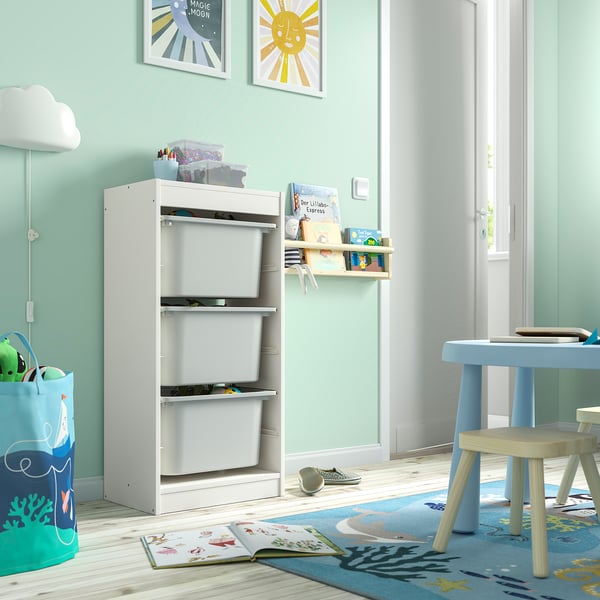 TROFAST hvide opbevaringsskuffer, vægside, legetøj i nærheden, på strandtæppe.