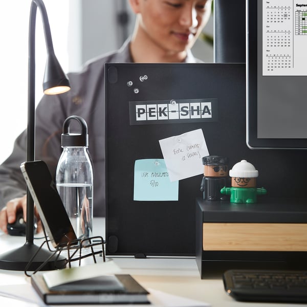 En arbejdsplads med en TROTTEN dobbeltsidet opslagstavle og whiteboard, monteret på et skrivebord. Den indeholder papirer, noter og små dekorationer, der hjælper med at organisere.