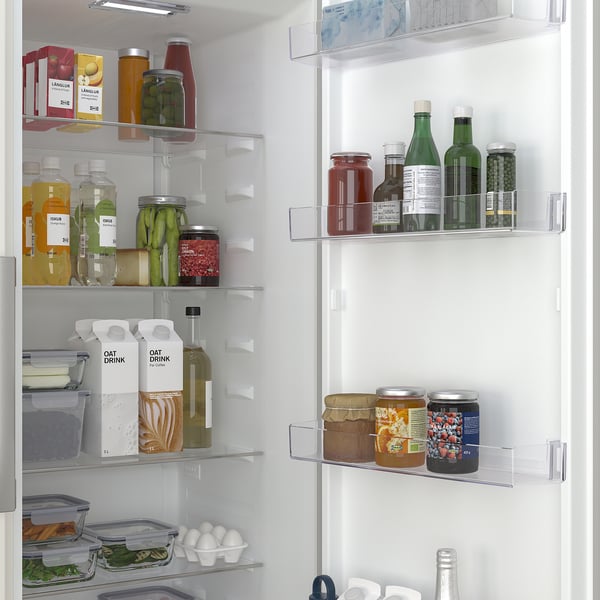 Organiseret køleskab med klare hylder, der viser forskellige madvarer, herunder frugt, grøntsager, drikkevarer og mejeriprodukter. En skarpere skuffe er synlig.