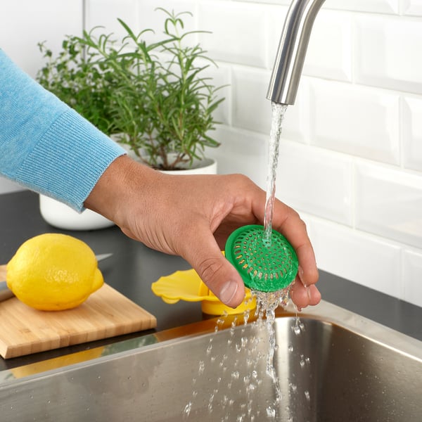 Person, der vasker en grøn citronpresser under vandhanen, med citron- og urtebaggrund.