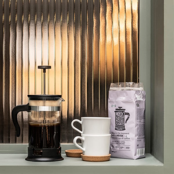 Sort stempelkande kaffemaskine med hvide krus og kaffepose i vindueskarmen.