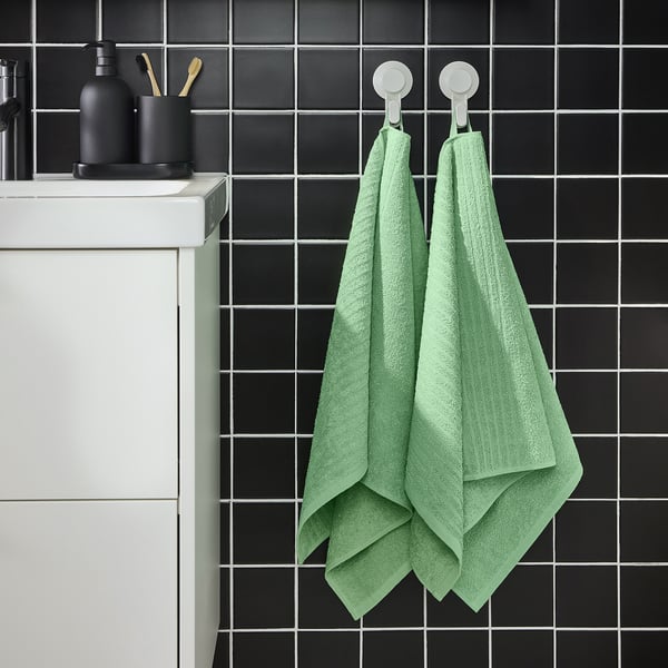 Moderne badeværelse med mørke fliser, hvidt skab og grønne VÅGSJÖN håndklæder. De er lette og absorberende og lyser rummet op.