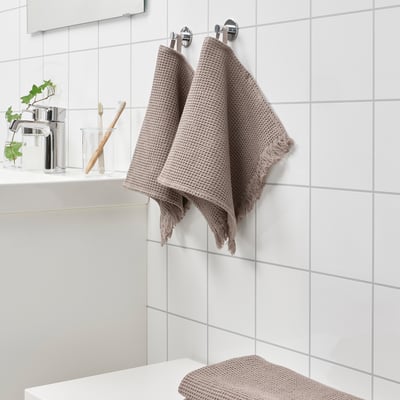 Lysebrunt VALLASÅN håndklæde hænger nær vasken; mindre end tandbørsteholder.