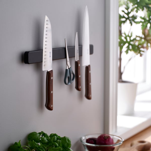 Magnetisk knivstativ rummer flere knive, sakse og en skræller på en væg, hvilket holder bordpladerne frie.