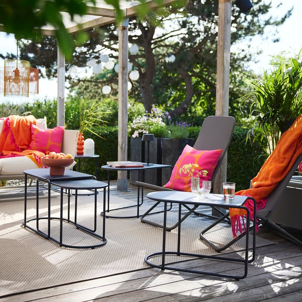 Terrasse med foldbare stole, puder, borde med glas og frugt, omgivet af planter og en pergola.