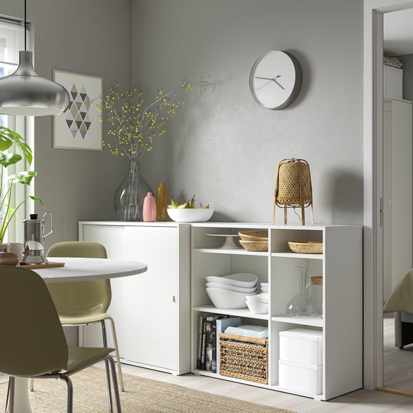 Moderne spiseplads med hvid VIHALS opbevaringsenhed. Hylder med skåle, vaser og indretning. Grønne stole, grå væg og ur ovenover.