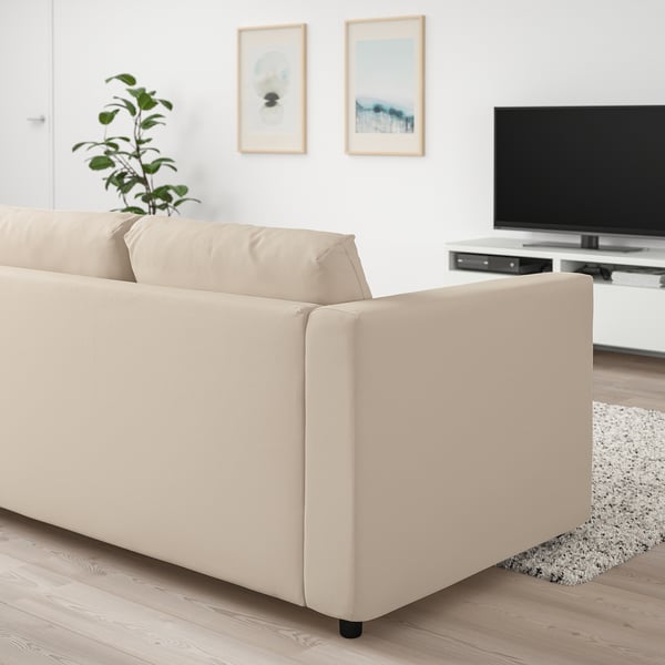 En beige VIMLE sofa i en stue. Det er en 3-personers sofa med et minimalistisk design, moderne linjer og er større end de omkringliggende indretningsgenstande.
