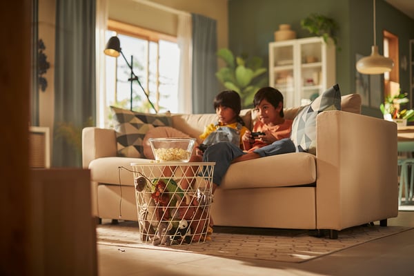 Børn leger på VIMLE sofa med snacks og planter i solrige rum.