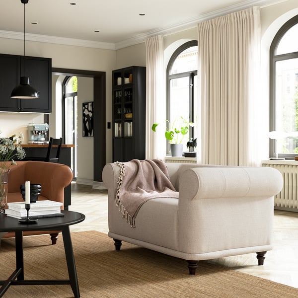 Moderne stue med beige VISKAFORS lænestol, ruststol, sort sofabord og buede vinduer med gardiner.