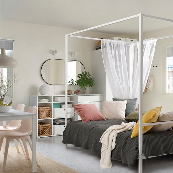 En himmelseng fra VITARNA med gardiner, gråt sengetøj og farverige puder i et lille, stilfuldt soveværelse. Den har opbevaring nedenunder.