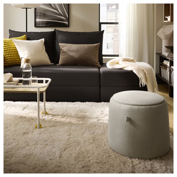 Moderne stue med sort sofa, hvidt shaggy tæppe og oval skammel. Accent med puder, et sidebord og et hyggeligt tæppe.