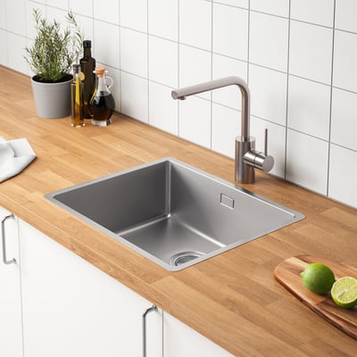 Moderne køkkenvask med vandhane i rustfrit stål, bordplade i træ og flasker, limefrugter og planteindretning.