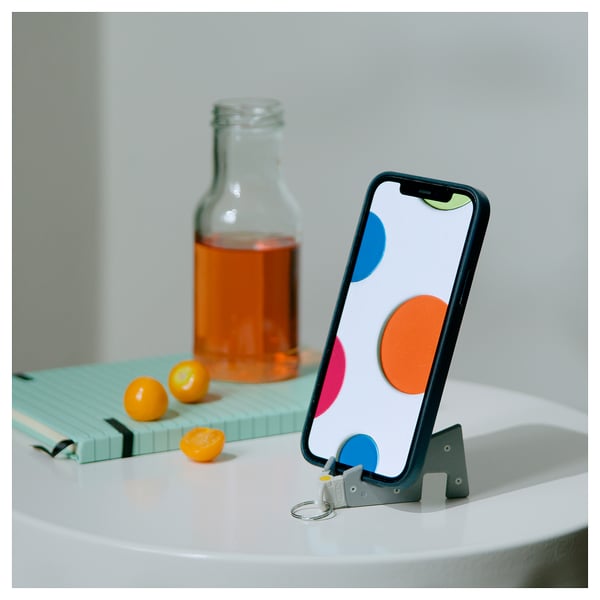 Sort og grå telefonholder med prikker, på hvidt bord med drink og frugt.